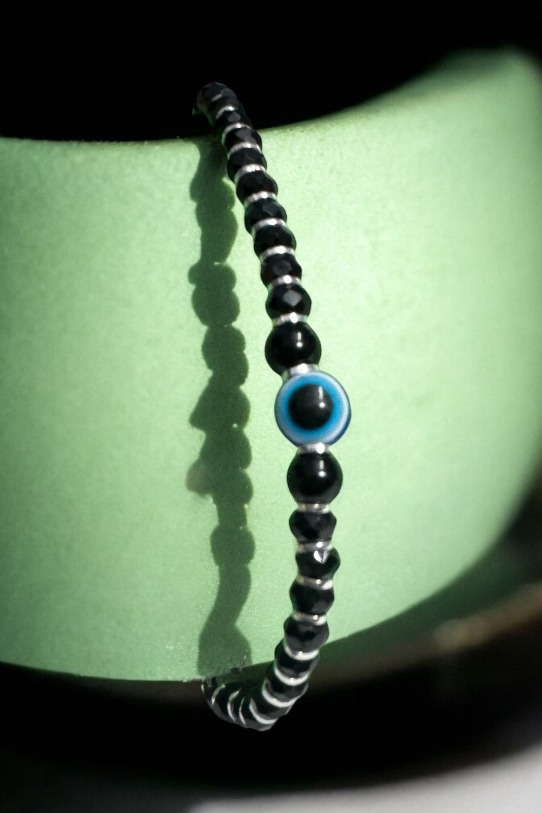 Black beaded bracelet with a blue eye charm on a wrist against a neutral background
