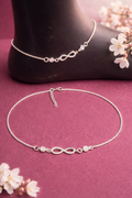 Silver anklets with infinity symbol on a pink surface with flowers