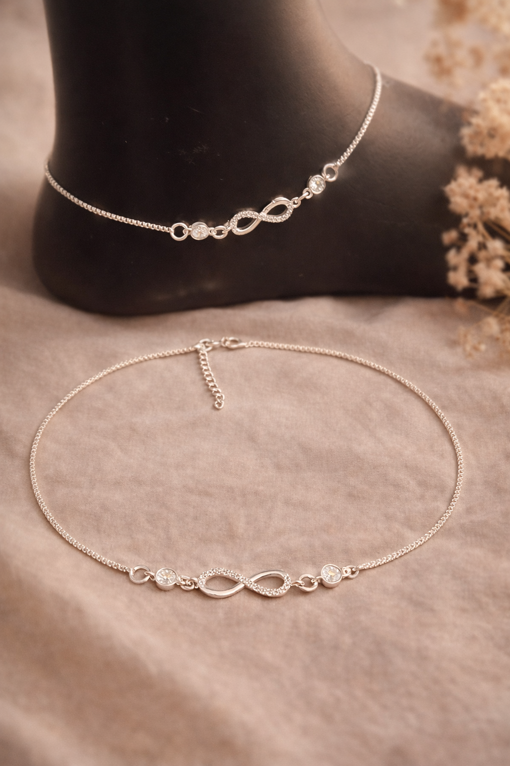 Silver anklets with infinity symbol design on a neutral background
