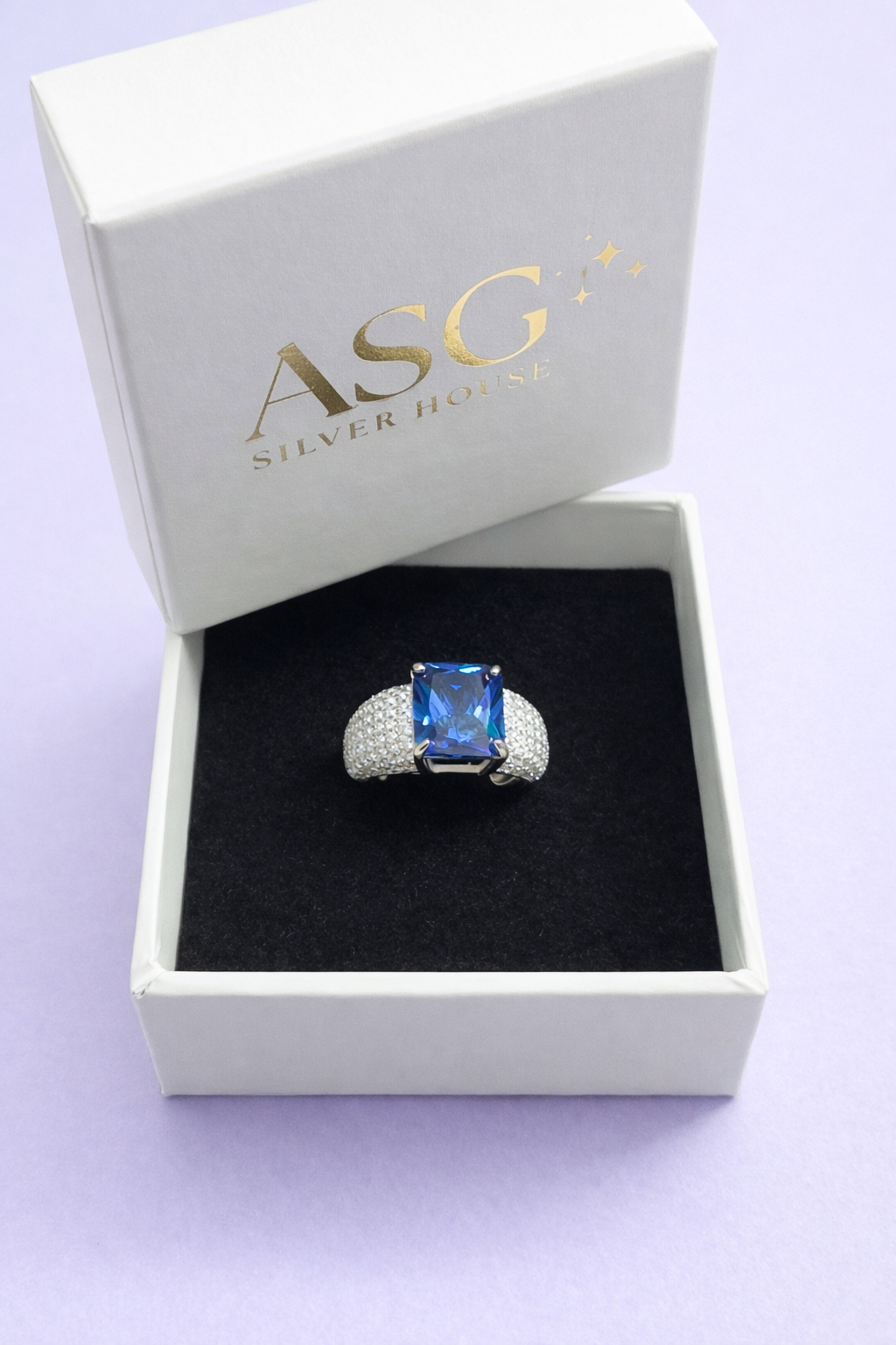 Silver ring with a blue gemstone in an open box with 'ASG Silver House' branding on a light purple background.