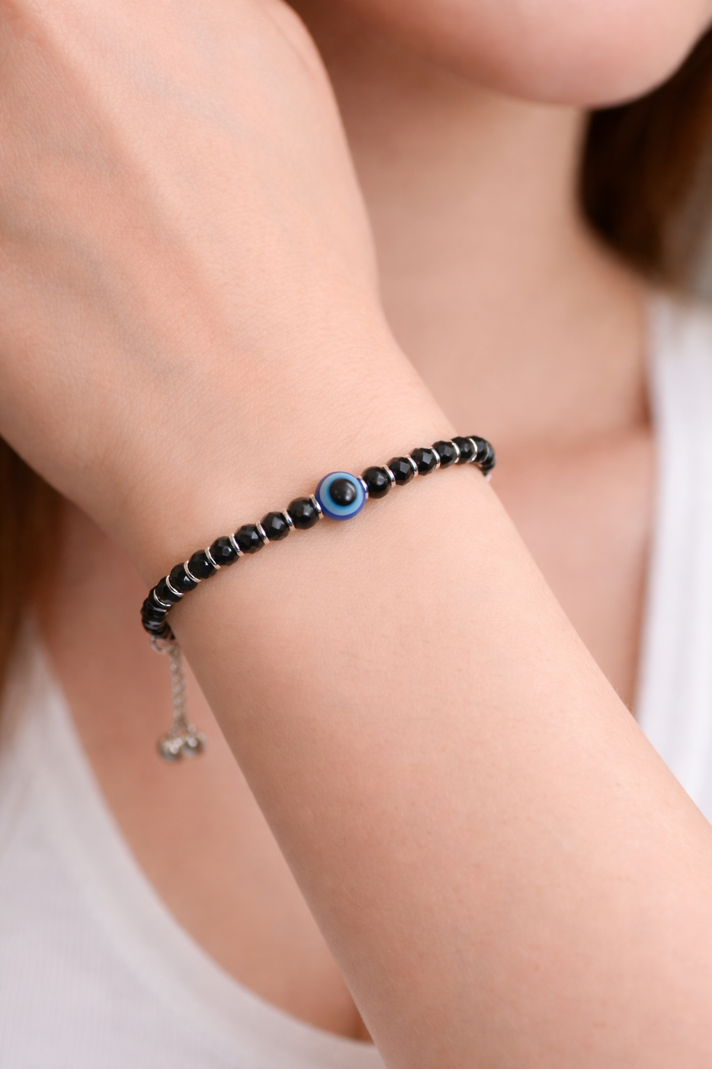 Black beaded bracelet with a blue eye charm on a wrist against a neutral background
