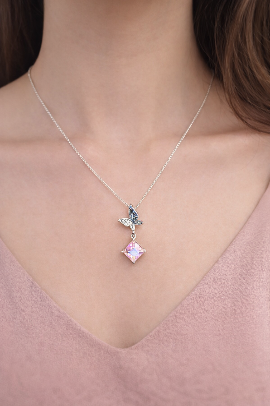 Necklace with a pink gemstone and butterfly pendant on a person wearing a pink top.