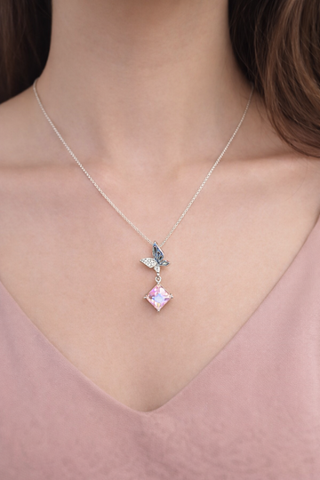 Necklace with a pink gemstone and butterfly pendant on a person wearing a pink top.