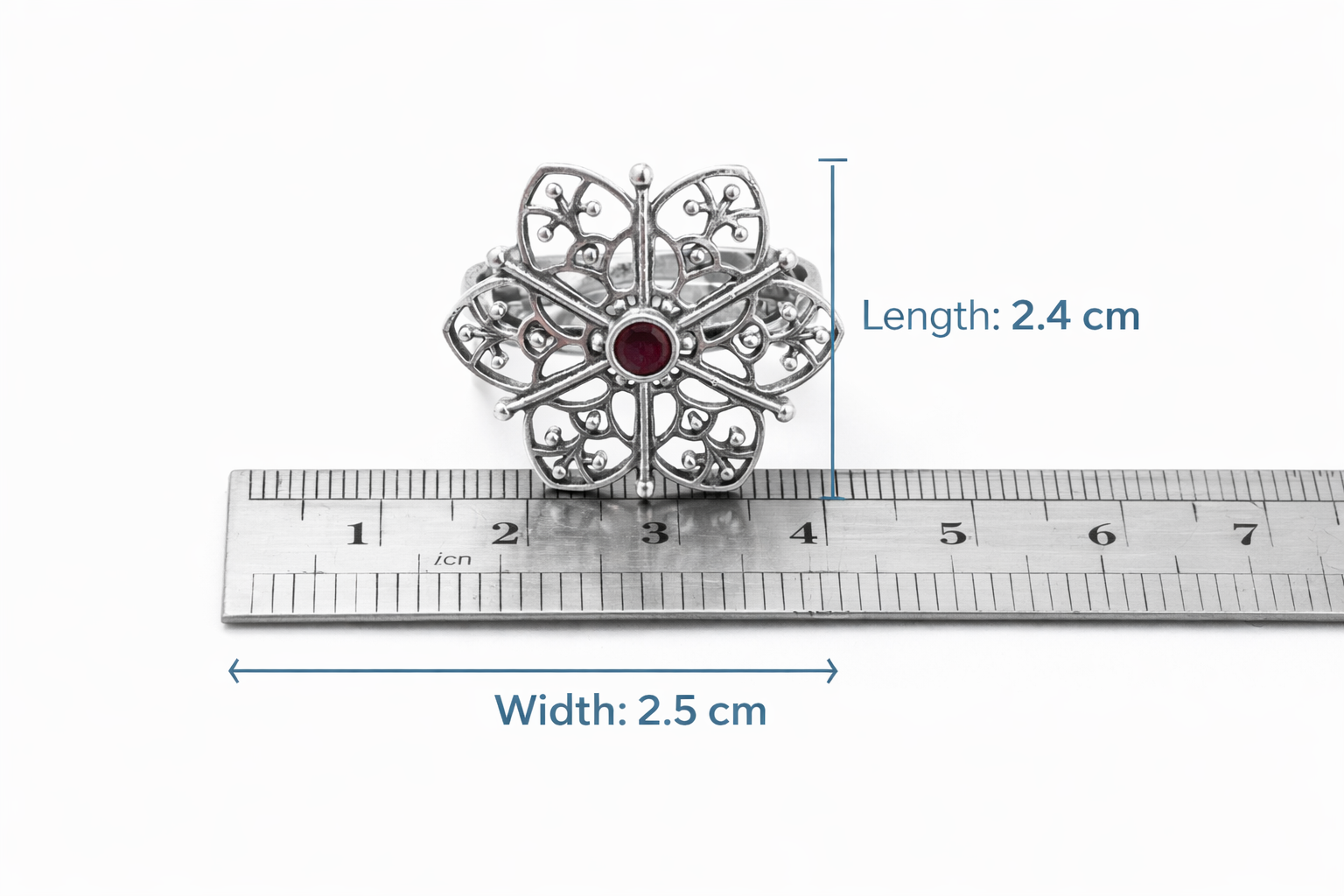 Silver brooch with a red gemstone next to a ruler showing its dimensions on a white background