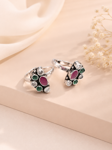 Two silver rings with green and red gemstones on a beige fabric background