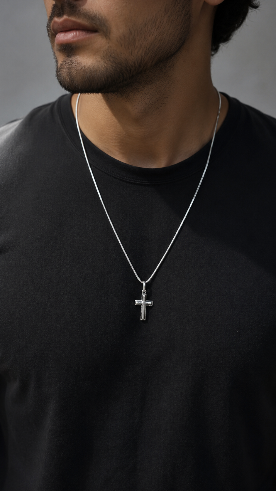 Man wearing a black shirt with a silver cross necklace against a dark background
