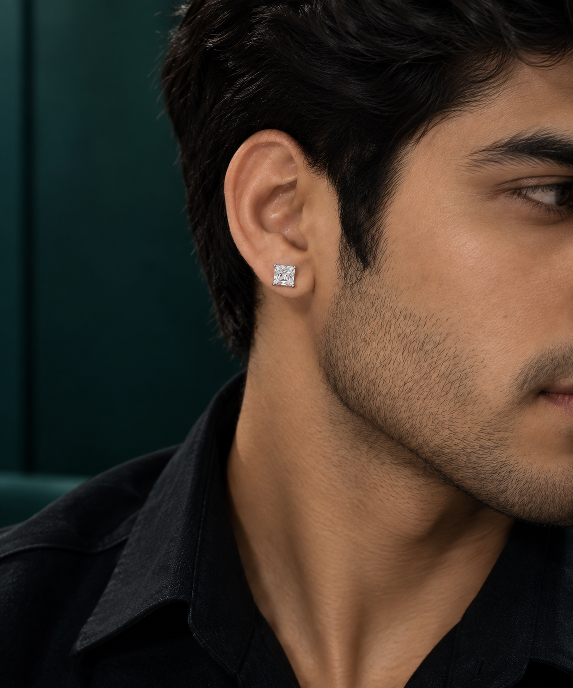 A close-up side profile of a man wearing a small square diamond stud earring in a dark green setting.
