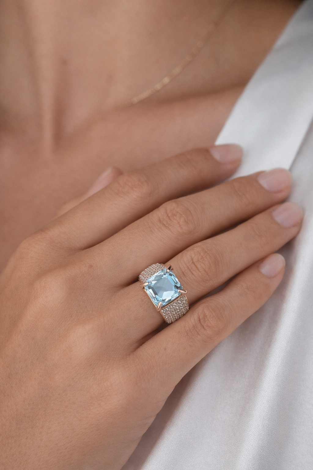 Hand wearing a ring with a blue gemstone on a neutral background