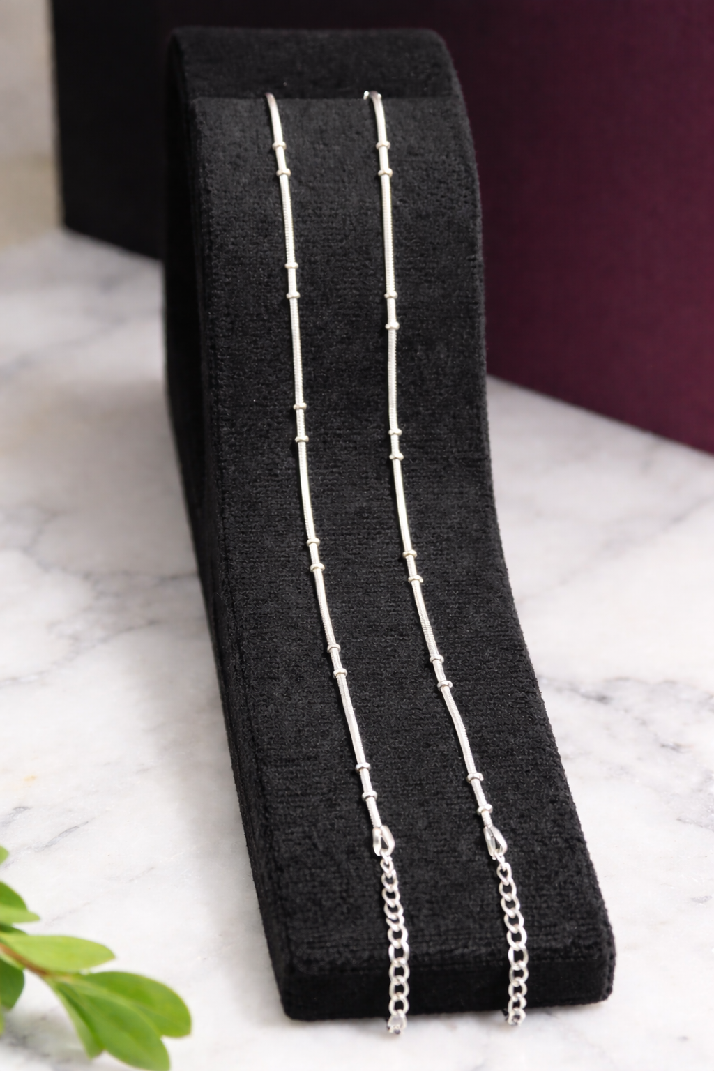 Silver Anklets a black stand with a marble backgroundt