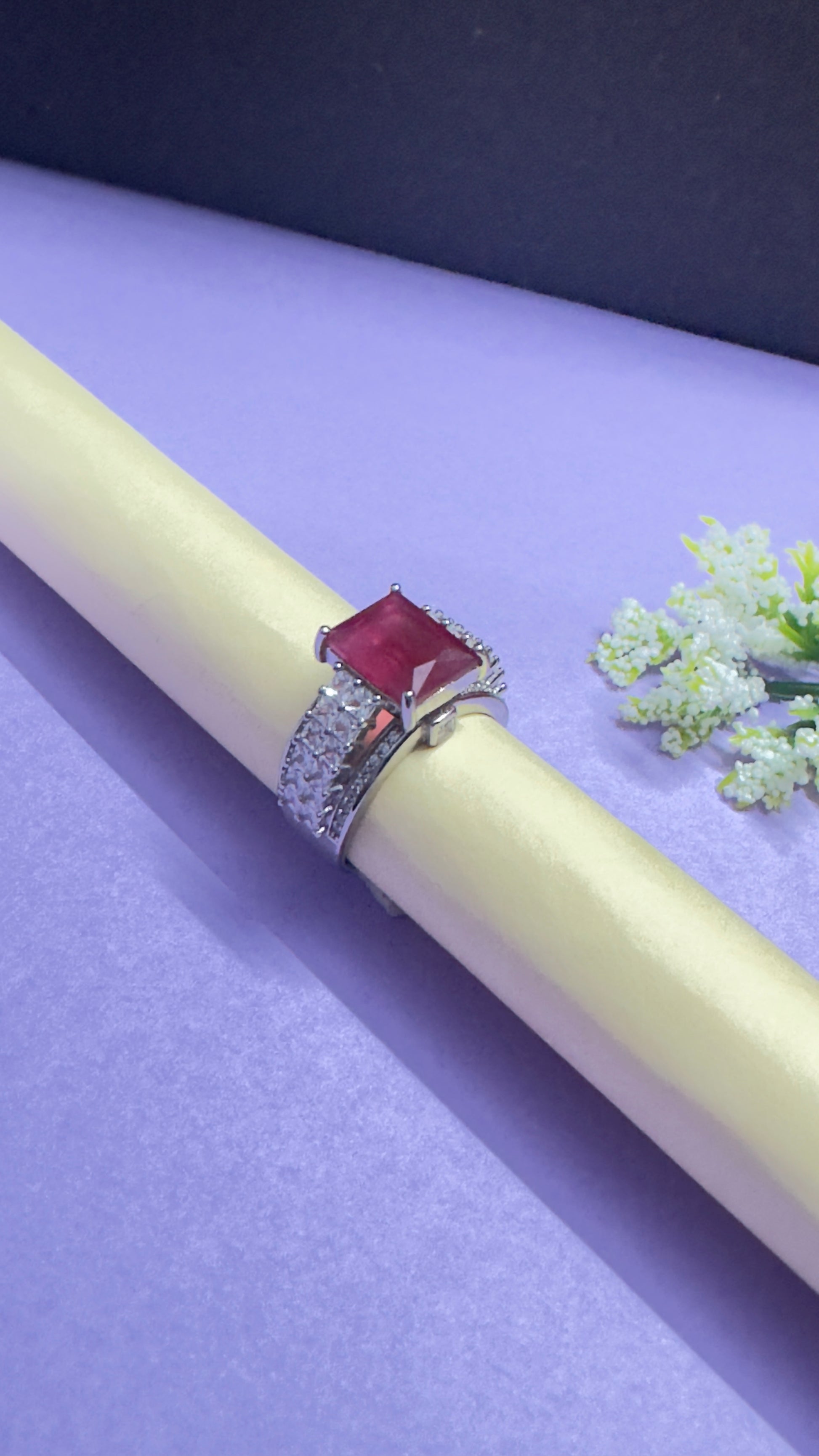Ring with a red gemstone on a white stick against a purple background