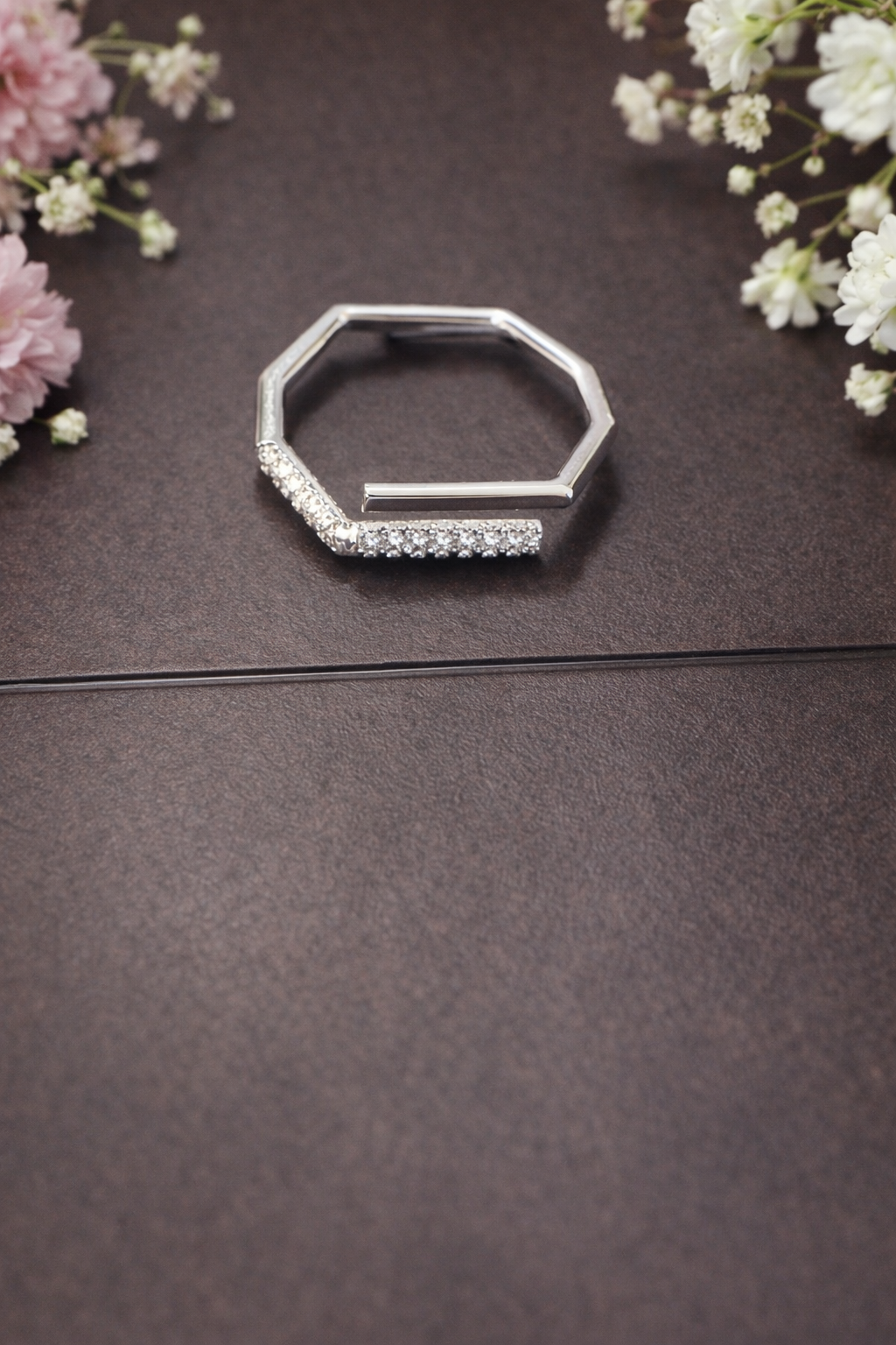 Silver ring with gemstones on a dark surface with flowers