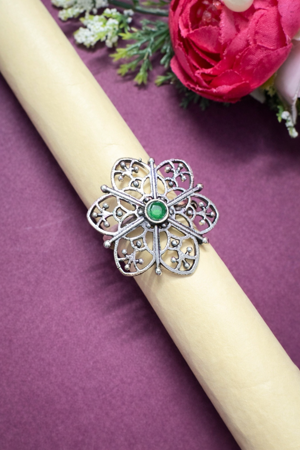 Silver ring with a green gemstone on a white candle against a purple background