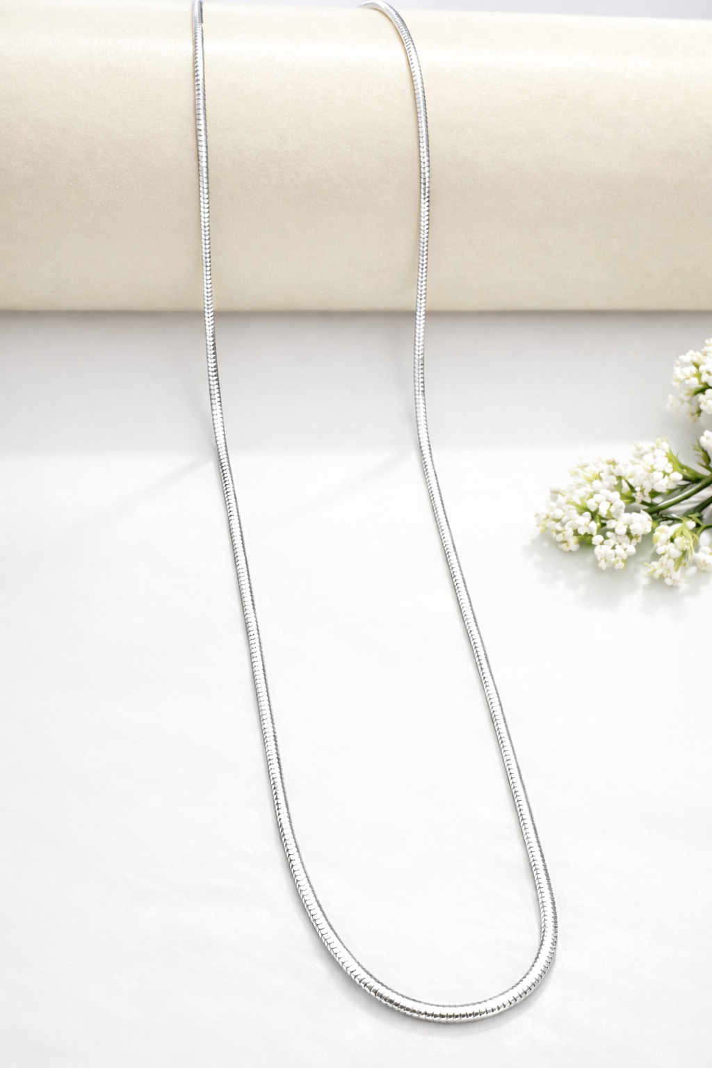 Silver necklace on a white surface with a beige background