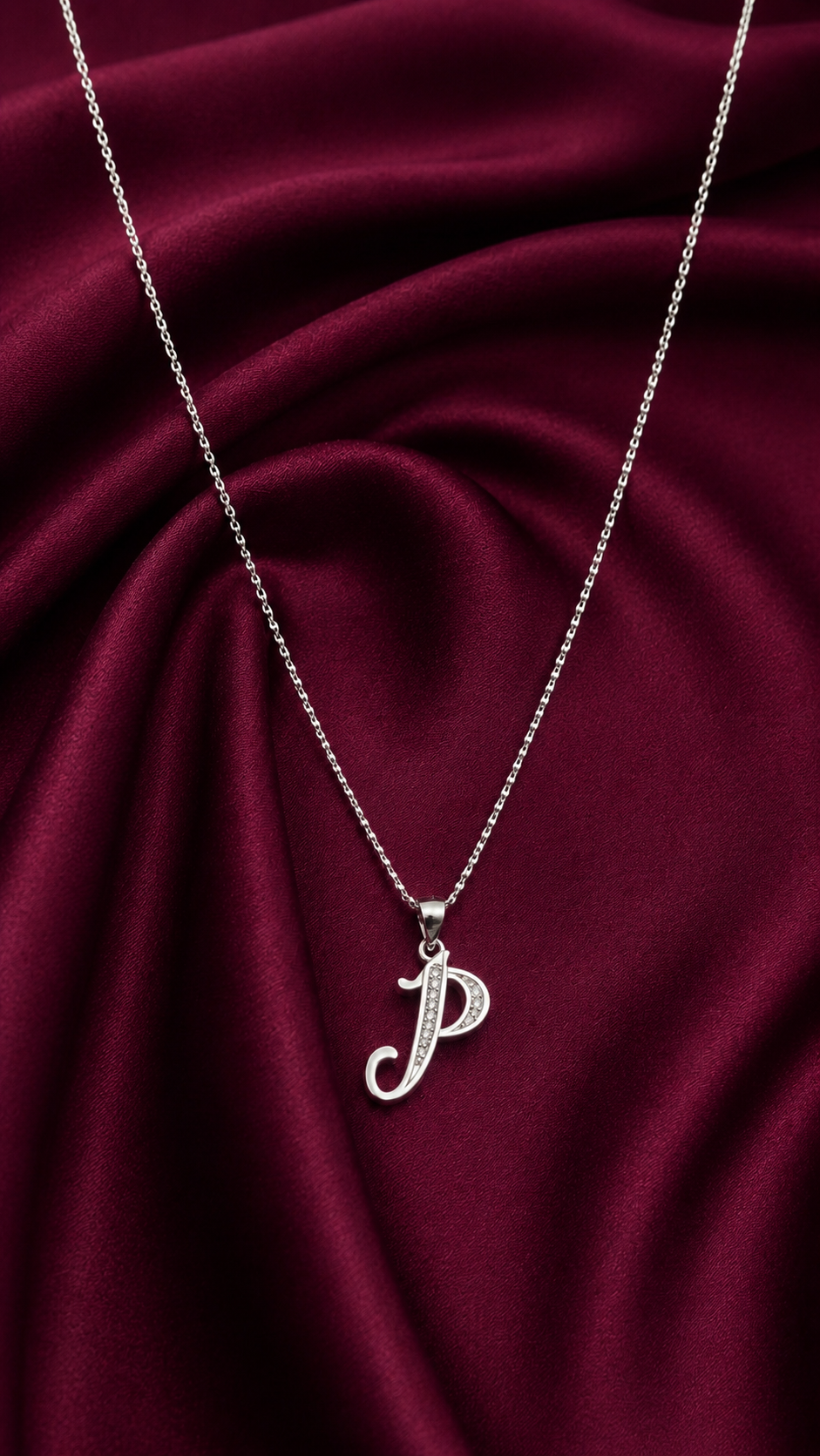 Silver necklace with a 'P' pendant on a burgundy fabric background